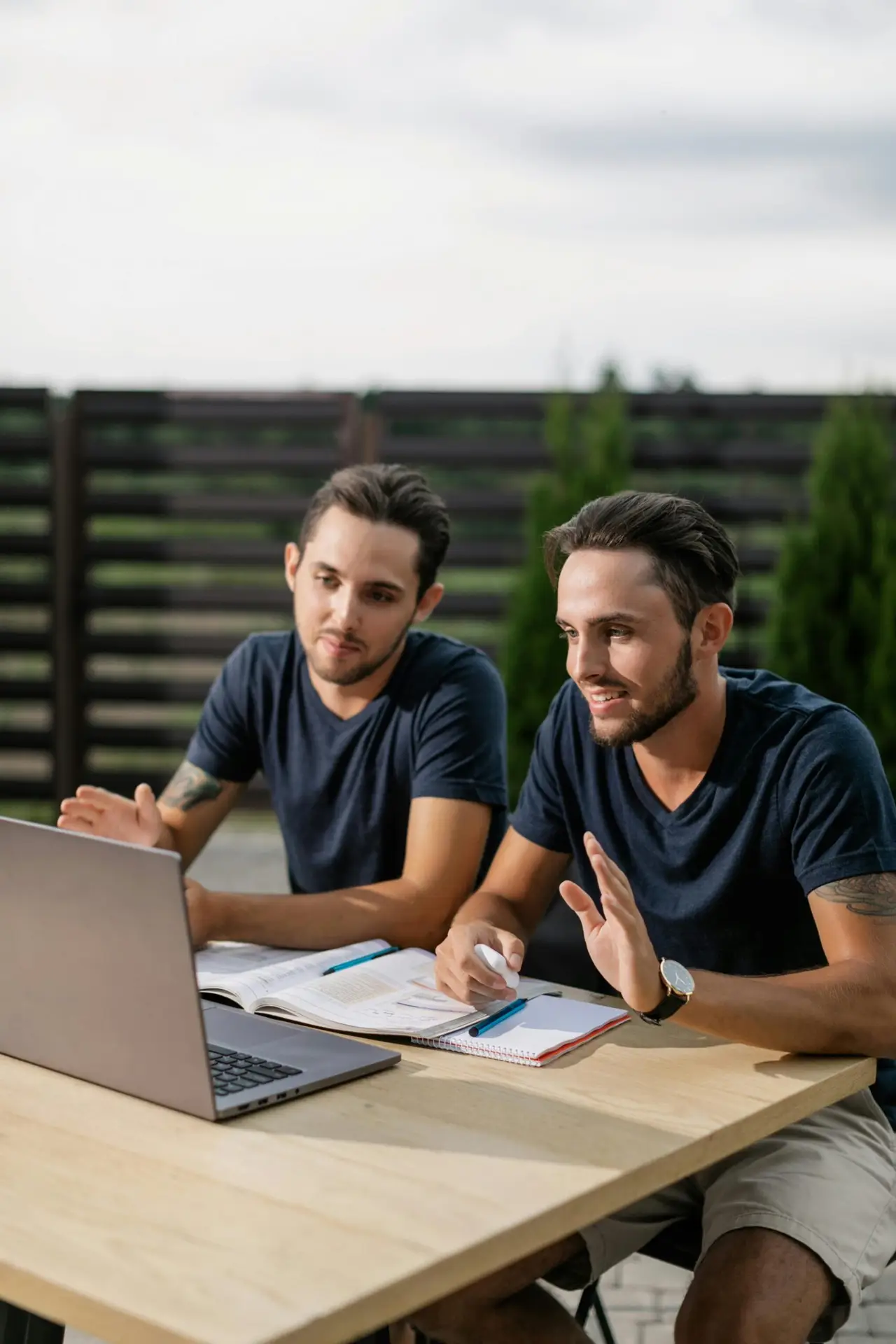 Two twin brothers engaging in online learning outdoors on a laptop.